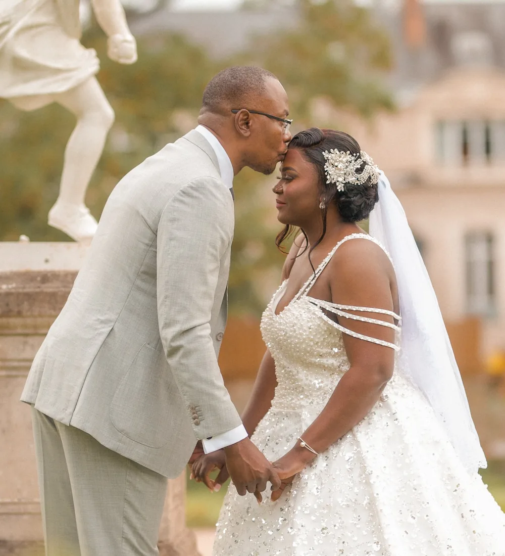 Le marié embrasse le front de la mariée devant une statue