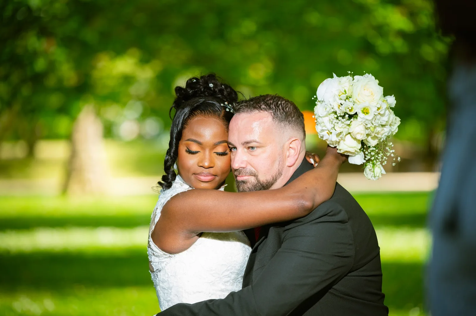Des mariés enlacés dans un parc, la mariée tenant son bouquet levé